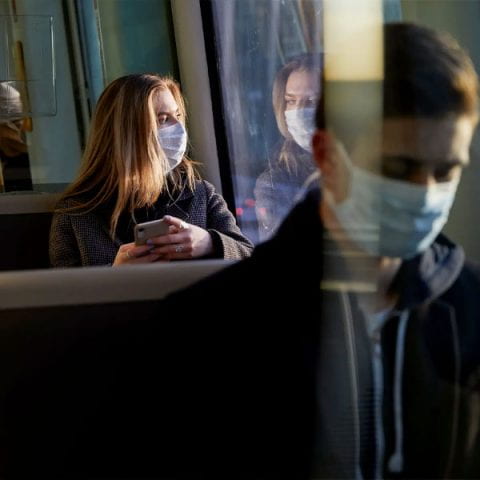 a woman looks out the window with a phone in her hand while riding public transportation